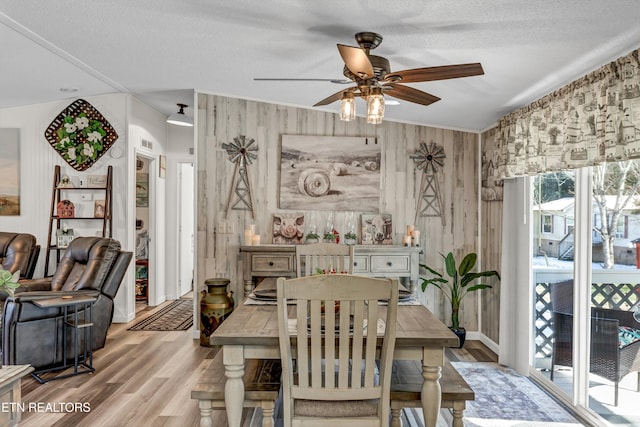 dining room featuring ceiling fan, light wood-type flooring, wooden walls, and a textured ceiling