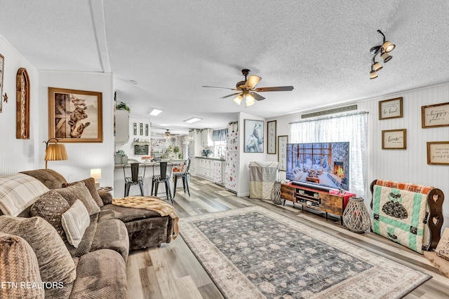 living room featuring light hardwood / wood-style floors, a textured ceiling, and ceiling fan