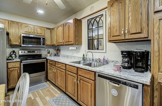 kitchen with light stone countertops, appliances with stainless steel finishes, ceiling fan, sink, and light hardwood / wood-style flooring