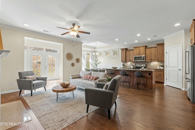 living room with sink, ceiling fan with notable chandelier, dark wood-type flooring, and ornamental molding