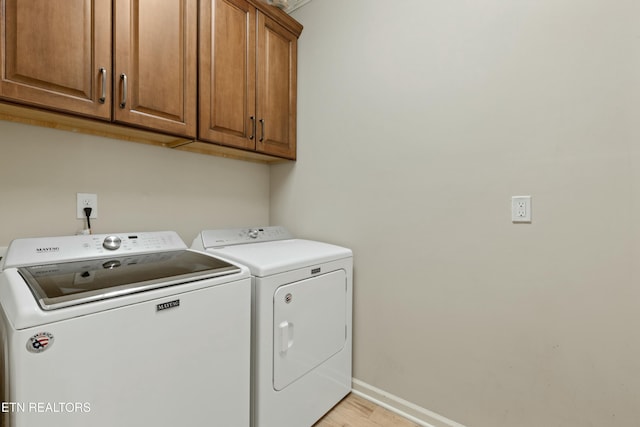 clothes washing area with washer and dryer, light hardwood / wood-style flooring, and cabinets