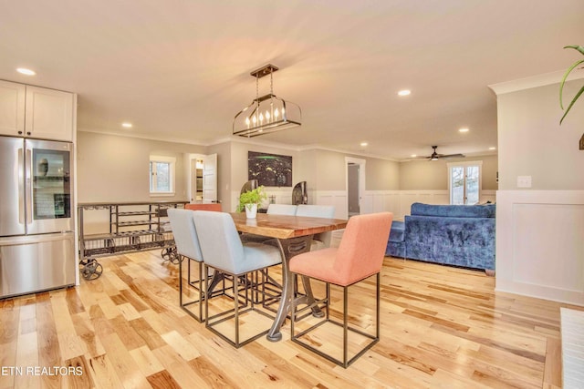 dining area with ceiling fan with notable chandelier, ornamental molding, and light hardwood / wood-style flooring