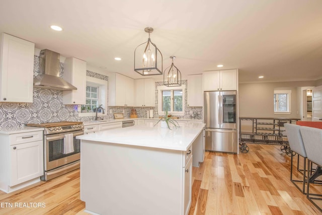 kitchen with white cabinets, appliances with stainless steel finishes, a kitchen island, and wall chimney exhaust hood