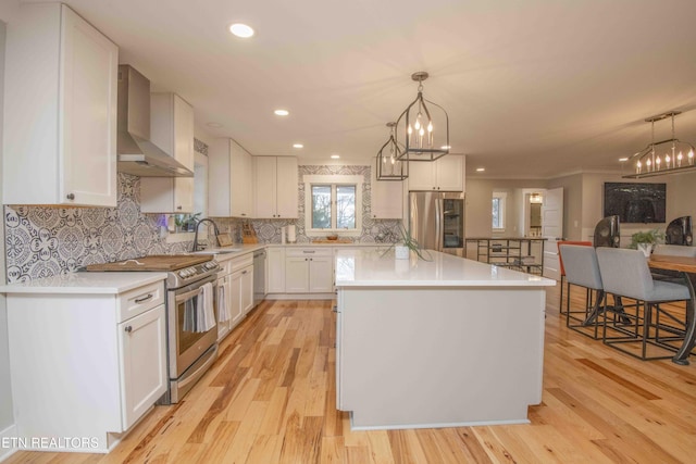 kitchen with appliances with stainless steel finishes, sink, wall chimney range hood, a center island, and white cabinetry