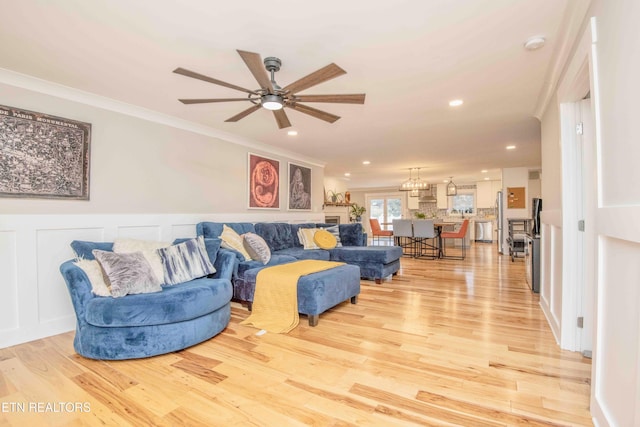 living room featuring ceiling fan with notable chandelier, light hardwood / wood-style floors, and ornamental molding