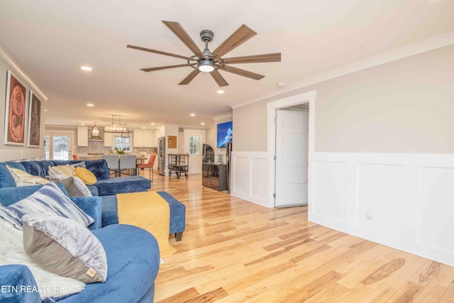 living room featuring light wood-type flooring, ceiling fan, and crown molding