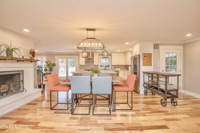 dining room featuring light hardwood / wood-style floors, a brick fireplace, a wealth of natural light, and crown molding