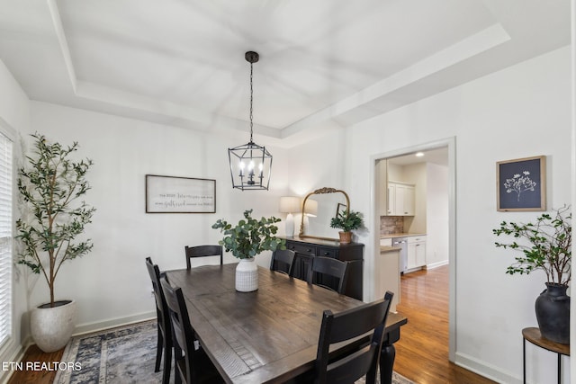 dining area with hardwood / wood-style floors, an inviting chandelier, and a tray ceiling