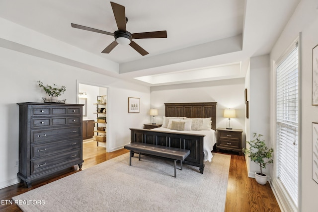 bedroom featuring ceiling fan, a raised ceiling, wood-type flooring, and ensuite bathroom