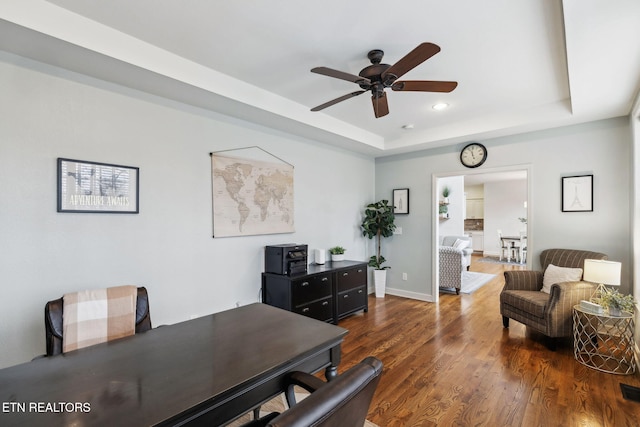 office with ceiling fan, dark wood-type flooring, and a tray ceiling