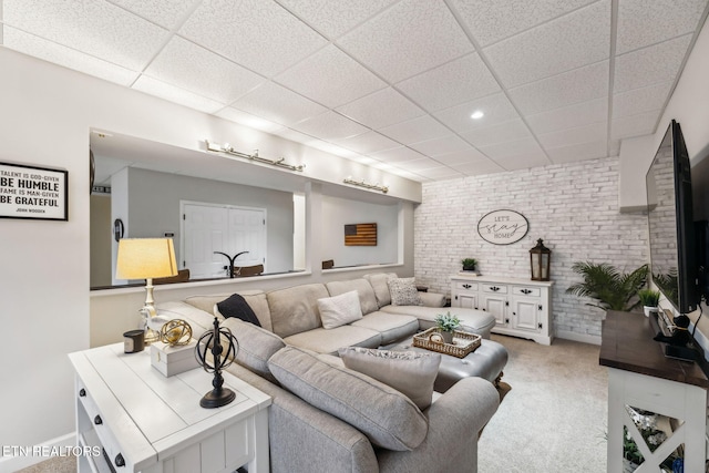 carpeted living room featuring a paneled ceiling and brick wall