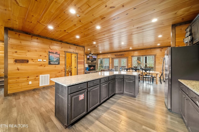 kitchen featuring wood ceiling, dark brown cabinetry, wooden walls, a kitchen island, and stainless steel refrigerator