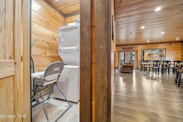 clothes washing area with french doors, wood ceiling, wooden walls, light hardwood / wood-style flooring, and stacked washer and clothes dryer