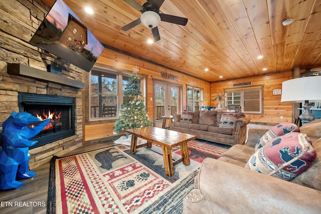 living room featuring wood ceiling, ceiling fan, wooden walls, wood-type flooring, and a stone fireplace