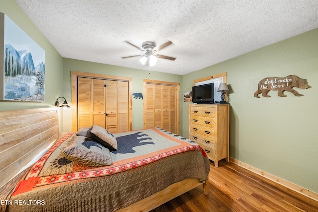 bedroom featuring two closets, a textured ceiling, hardwood / wood-style flooring, and ceiling fan