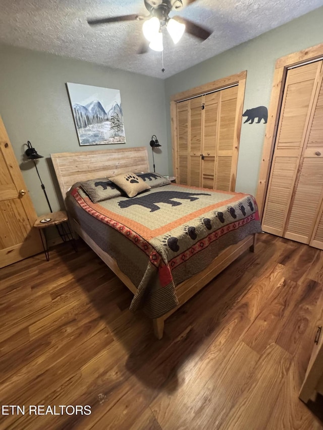 bedroom featuring a textured ceiling, a ceiling fan, dark wood finished floors, and two closets