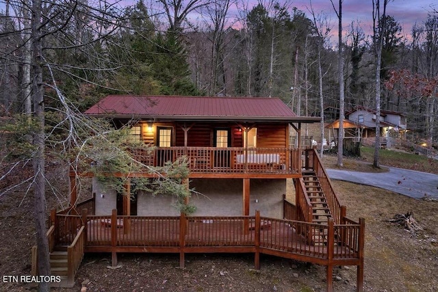 rear view of property with stairs, covered porch, a deck, metal roof, and a wooded view