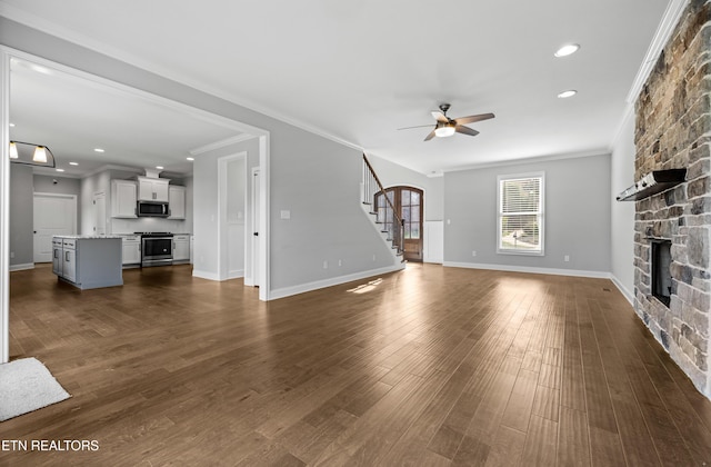 unfurnished living room with a stone fireplace, ceiling fan, crown molding, and dark hardwood / wood-style flooring