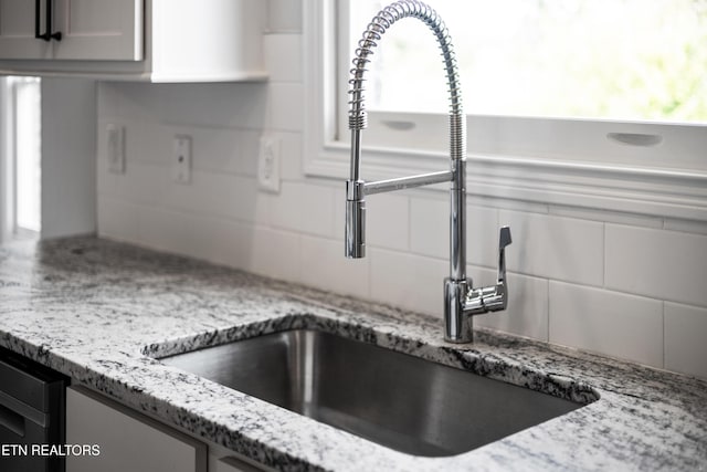 kitchen featuring tasteful backsplash, light stone counters, and sink