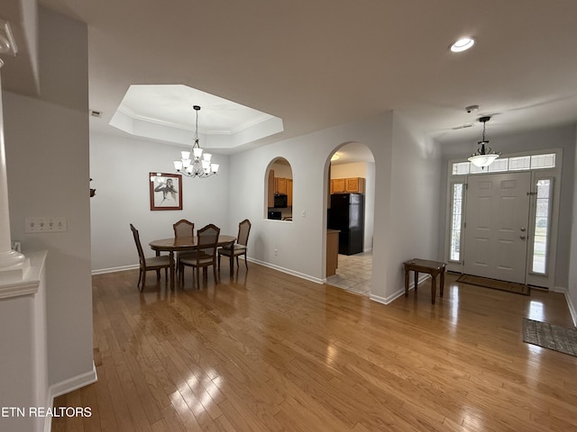 dining room featuring a tray ceiling, light hardwood / wood-style flooring, a notable chandelier, and crown molding