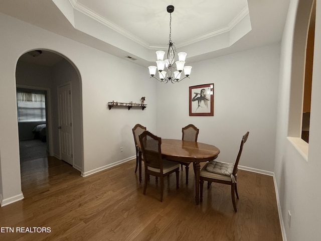 dining space featuring a tray ceiling, dark wood-type flooring, a chandelier, and ornamental molding