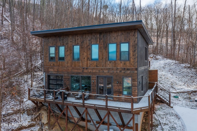 snow covered back of property with a wooden deck and french doors