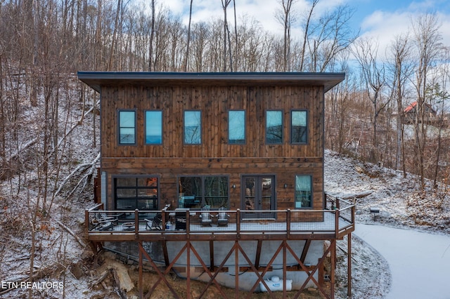 snow covered back of property with french doors and a wooden deck