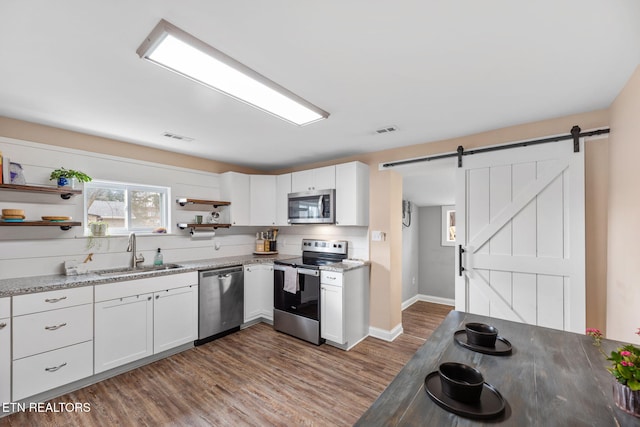 kitchen featuring stainless steel appliances, sink, white cabinetry, a barn door, and dark hardwood / wood-style flooring