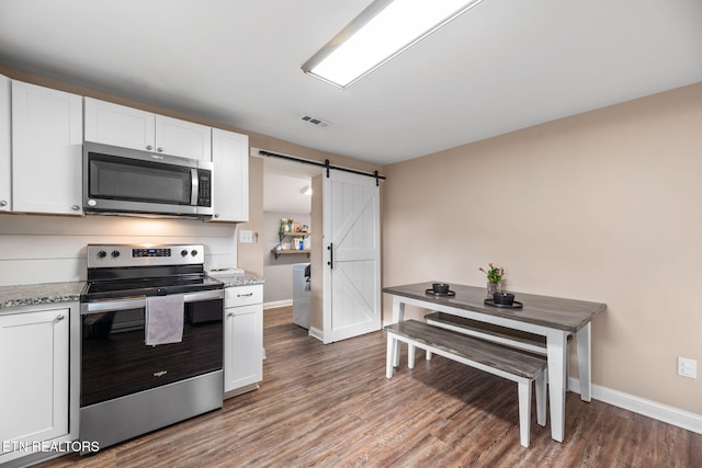 kitchen with appliances with stainless steel finishes, white cabinets, a barn door, and light stone counters