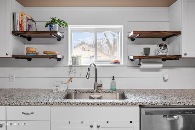 kitchen with sink, wooden walls, white cabinetry, stainless steel dishwasher, and light stone countertops