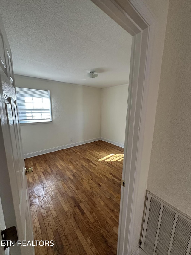 empty room with wood-type flooring and a textured ceiling