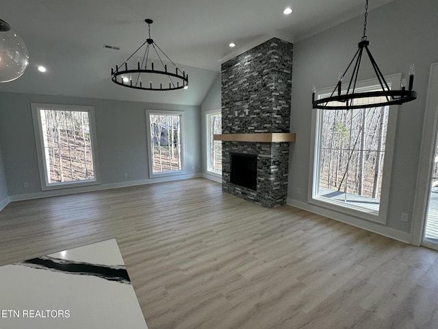 unfurnished living room with a stone fireplace, light hardwood / wood-style floors, vaulted ceiling, and a notable chandelier