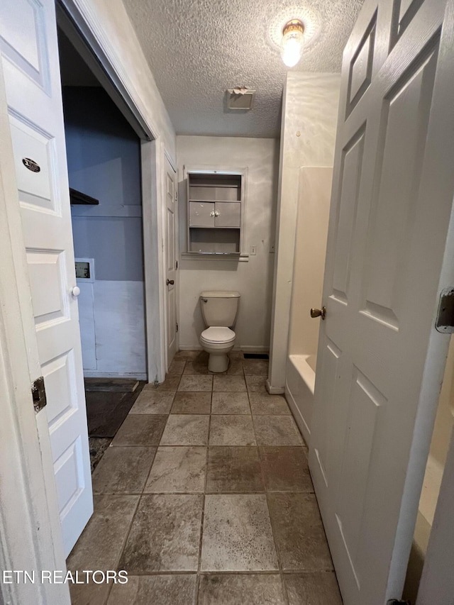 full bathroom featuring a tub, baseboards, a textured ceiling, and toilet