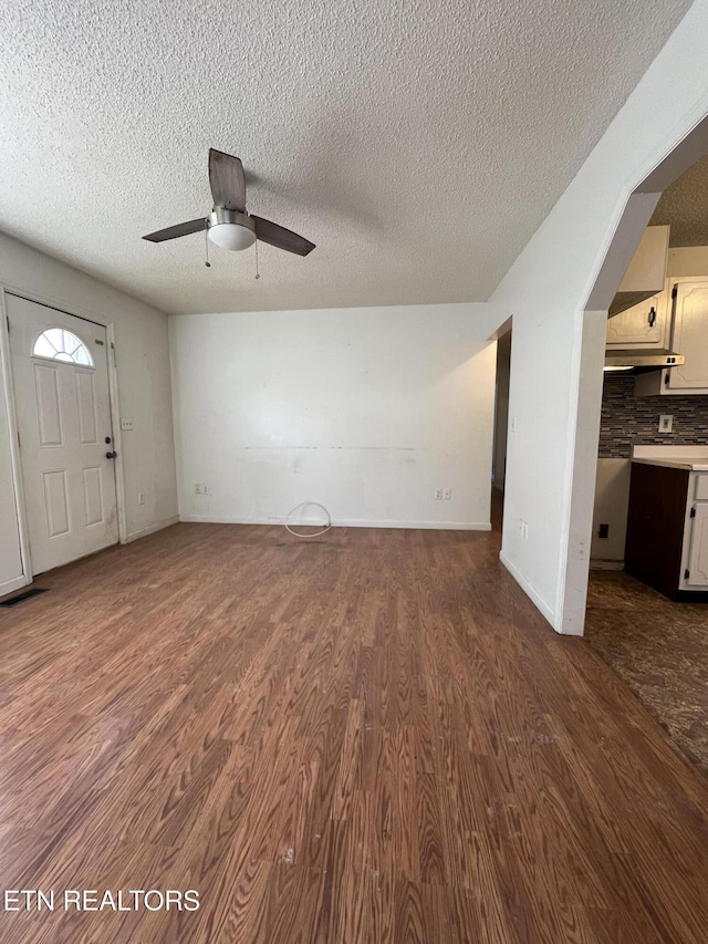 unfurnished living room with ceiling fan, a textured ceiling, wood finished floors, and baseboards