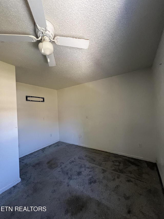 spare room featuring a textured ceiling, dark carpet, and a ceiling fan