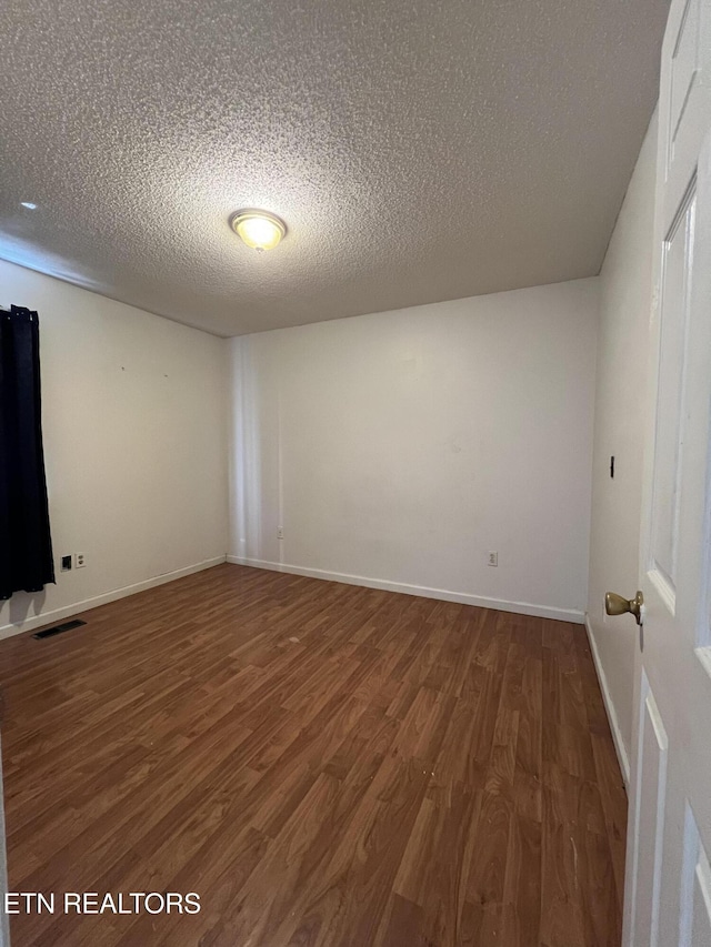 spare room featuring baseboards, a textured ceiling, visible vents, and wood finished floors