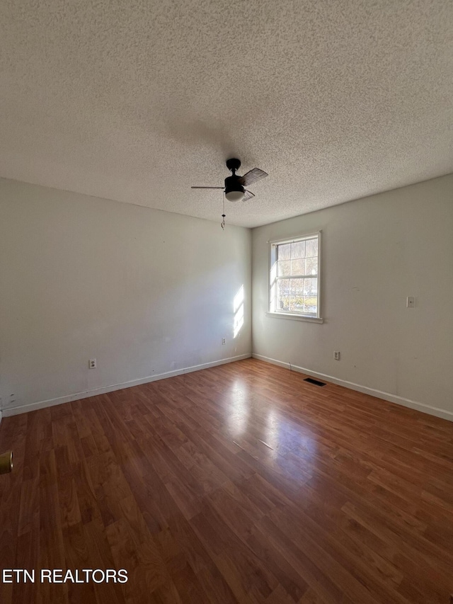 spare room with dark wood-type flooring, visible vents, ceiling fan, and baseboards