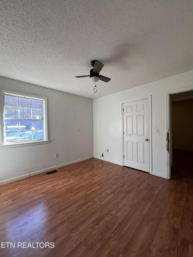 unfurnished bedroom featuring baseboards, a textured ceiling, visible vents, and dark wood-style flooring