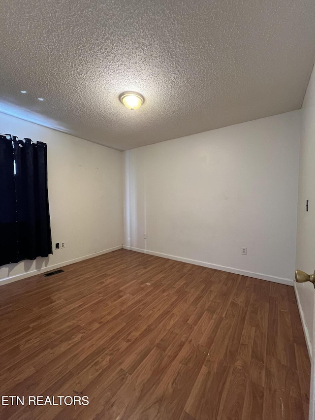 spare room with a textured ceiling, wood finished floors, visible vents, and baseboards