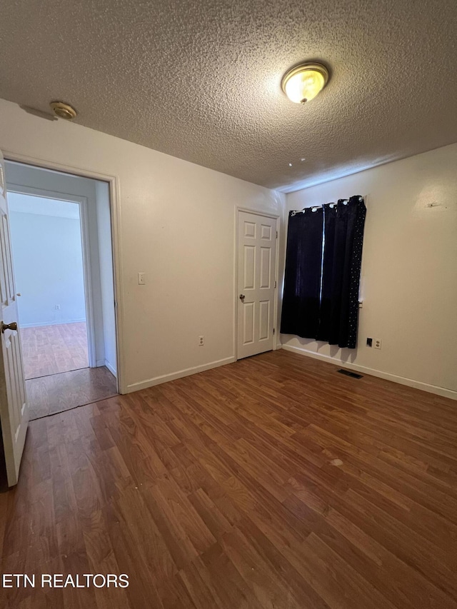 unfurnished room with baseboards, a textured ceiling, visible vents, and wood finished floors