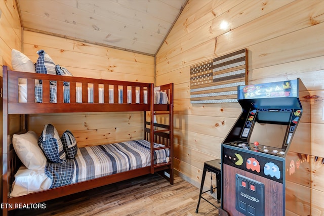 bedroom with lofted ceiling, wood-type flooring, and wooden walls