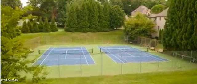 view of tennis court with a lawn and fence