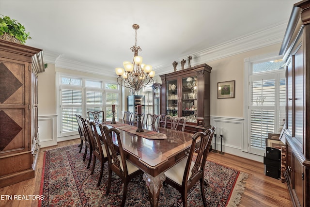 dining area with a notable chandelier, light wood-style flooring, crown molding, and a decorative wall