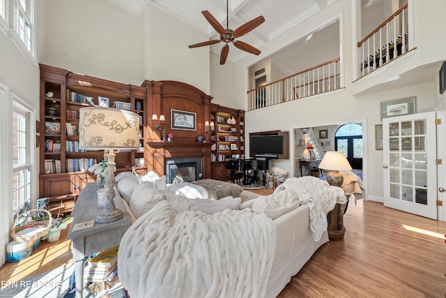 living room with a glass covered fireplace, ceiling fan, wood finished floors, and a healthy amount of sunlight