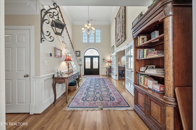 foyer featuring a wainscoted wall, a notable chandelier, ornamental molding, wood finished floors, and french doors