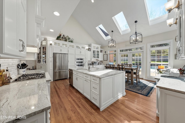 kitchen with a sink, hanging light fixtures, stainless steel appliances, light wood-style floors, and white cabinetry