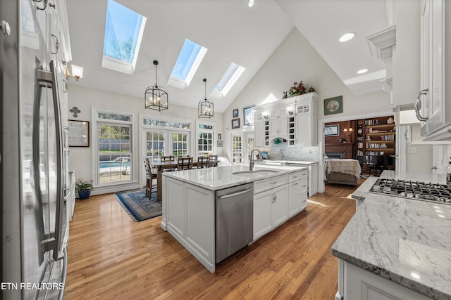 kitchen featuring a sink, white cabinetry, light wood-style floors, appliances with stainless steel finishes, and hanging light fixtures