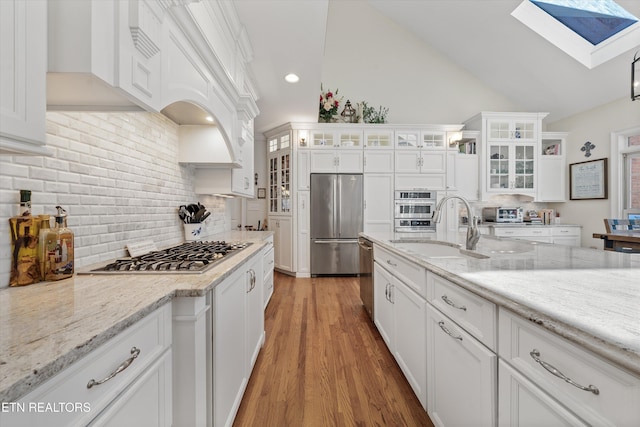 kitchen featuring light wood-style flooring, a sink, tasteful backsplash, appliances with stainless steel finishes, and white cabinets