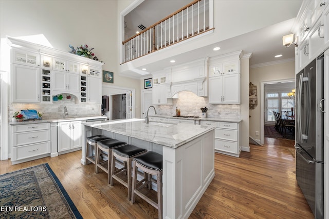 kitchen with a center island with sink, light wood-style flooring, stainless steel appliances, white cabinetry, and crown molding