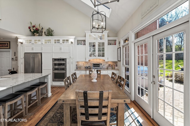 dining area featuring a toaster, lofted ceiling, french doors, wood finished floors, and a notable chandelier